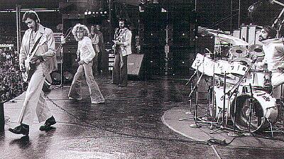 June 1976, with stage-left view of floor wedge monitors and dual foldback stacks behind John to the right of his Sunn/Stramp amp rack.