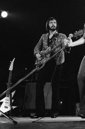 Ca. 1975, with Alembic Series 1 bass in zebra wood. Peter Cook “Lightning Bolt” bass headstock/neck visible on stand at left (as seen on cover of The Who By Numbers).