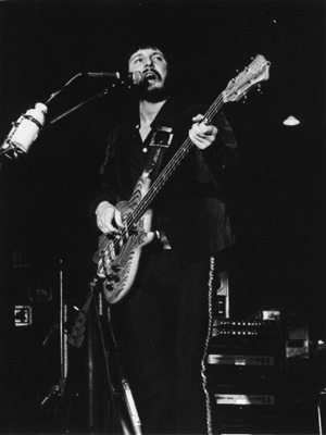 Ca. October 1975, with Alembic Series 1 bass in zebra wood. Alembic/Sunn Coliseum Power Amp amplifier rack visible at right. Peter Cook “Lightning Bolt” bass headstock/neck visible on stand at left (as seen on cover of The Who By Numbers).