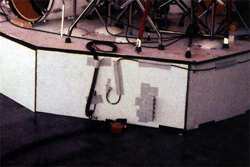 Ca. 1979, closeup view of Pete’s MXR Dyna-Comp pedal, set up in front of Kenney Jones’ riser. Note spare guitar and amp cables taped to riser.